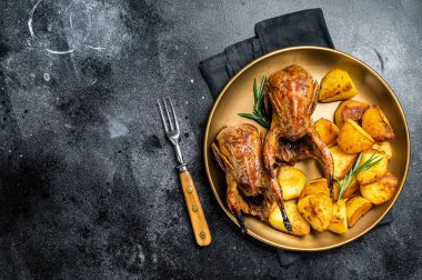 Delicious roasted quails with herbs in a plate with fried potato. Black background. Top view. Copy space.