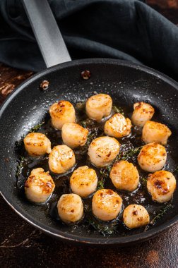 Fried scallops with butter lemon sauce in a skillet. Dark background. Top view.