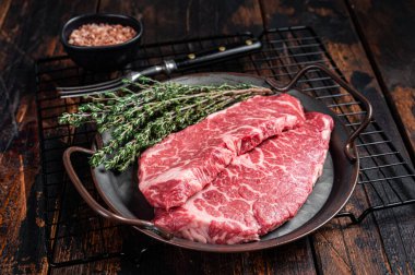 Fresh raw Denver Steak, beef meat with sea salt, seasonings and spices, ready to grill. Wooden background. Top view.