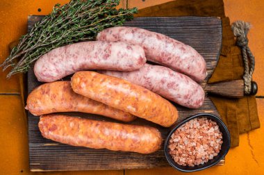 Fresh Raw Bratwurst and Chorizo meat sausages on wooden board. Orange background. Top view.