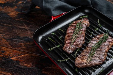Fried denver beef meat steak with thyme in a grill skillet. Wooden background. Top view. Copy space.