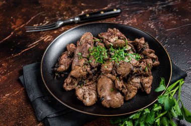 Fried chicken liver with onions and parsley in a plate. Dark background. Top view.