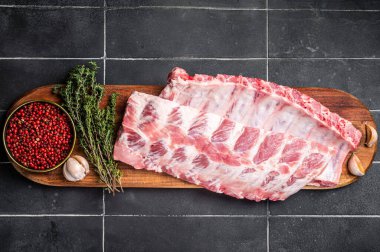 Fresh Pork Spareribs, Raw spare loin ribs on a wooden board with thyme and spices. Black background. Top view.