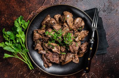 Fried chicken liver with onions and parsley in a plate. Dark background. Top view.