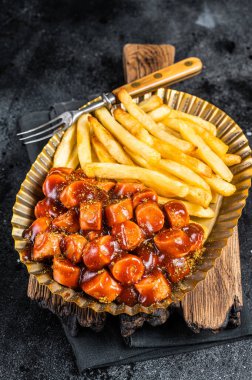 German currywurst with french fry served in a steel plate. Black background. Top view.