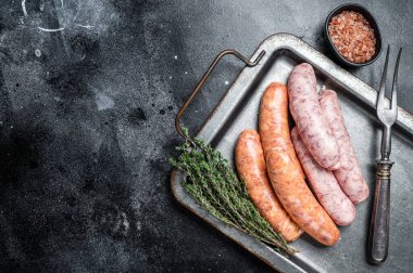 Raw barbecue sausages with spices in kitchen tray. Black background. Top view. Copy space.