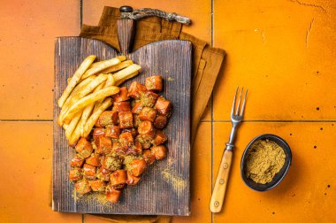 Curried sausage currywurst meal, curry wurst with french fry served on a wooden board. Orange background. Top view.