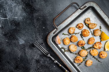 Scallops poached in a butter and garlic Sauce in a steel tray with thyme. Black background. Top view. Copy space.