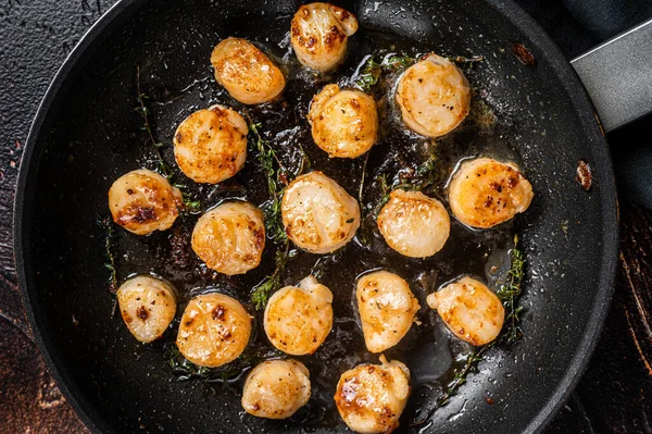Fried scallops with butter lemon sauce in a skillet. Dark background. Top view.