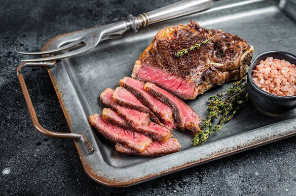 stock image Grilled Wagyu Striploin beef meat steak or new york steak in a steel tray. Black background. Top view.