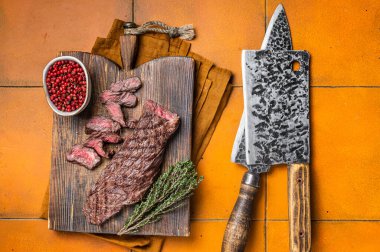 Grilled Medium Rare Machete or skirt beef meat steak on wooden cutting board. Orange background. Top view.