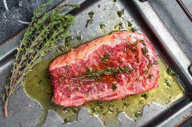Marinated Raw striploin, New york steak with olive oil, thyme and pepper. Black background. Top view.