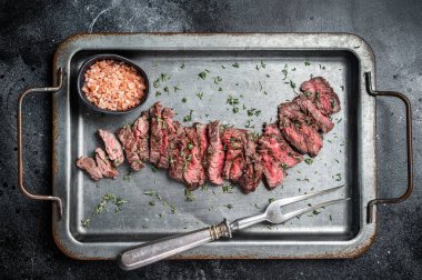 Grilled sliced Machete beef meat steak on steel tray with thyme. Black background. Top view.