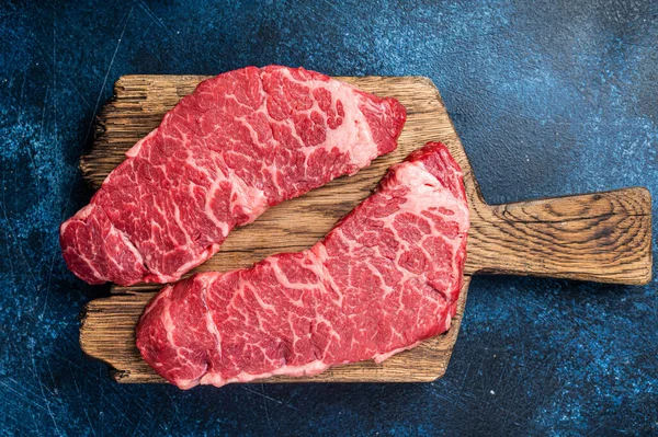 Alternative beef steak Denver, raw meat steak on a wooden board. Blue background. Top view. Copy space.