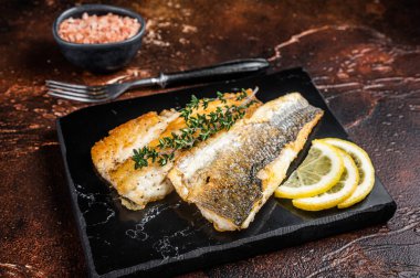 Roast sea bass fillet with lemon and thyme, seabass fish. Dark background. Top view.