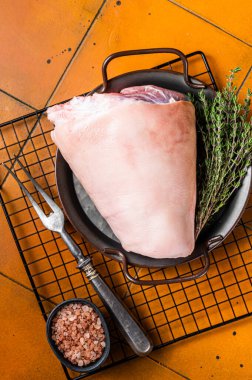 Raw pork shank knuckle in a steel tray with herbs. Orange background. Top view.