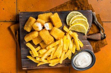 Fish and Chips British fastfood, Fish Sticks with french fries on wooden board. Orange background. Top view.