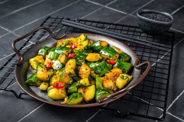 Chinese smashed cucumber salad with chili peppers and sesame seeds. Black background. Top view.