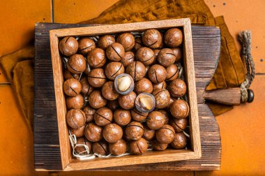 Macadamia natural nuts in a box. Orange background. Top view.