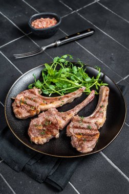 Roasted lamb meat cutlets, mutton chops with garnish. Black background. Top view.