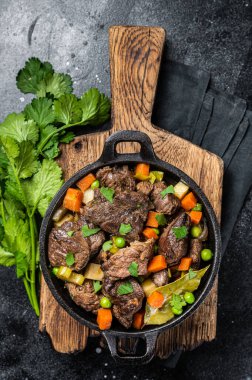 Beef stew with potato, carrot and herbs in a skillet. Black background. Top view.