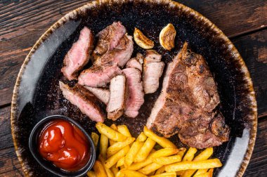 Roast BBQ pork chop steak on plate with potato chips. Wooden background. Top view.