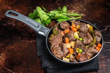 Irish stew with beef meat, potatoes, carrots and herbs in a skillet. Dark background. Top view.
