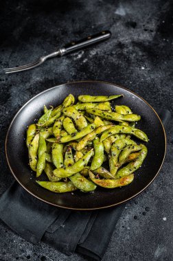 Stir-fried green Edamame Soy Beans with sea salt and sesame seeds in a plate. Black background. Top view.