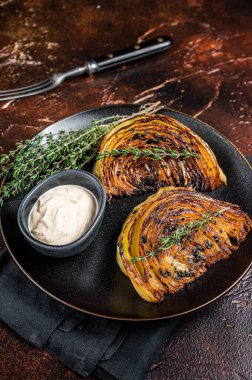 Vegan grilled cabbage steaks with sauce on a black plate. Dark background. Top view.