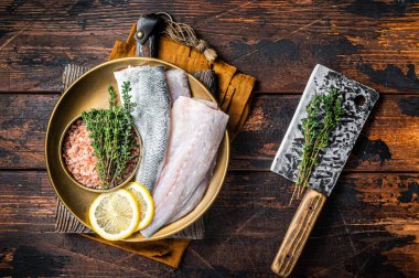 Uncooked Raw Sea Bass fillets, Seabass fish with thyme, pink salt and lemon. Dark background. Top view.