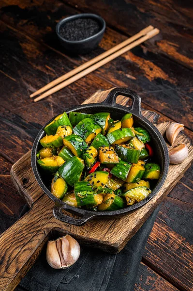 Chinese Smashed Cucumber salad pai huang gua in a skillet. Wooden background. Top view.