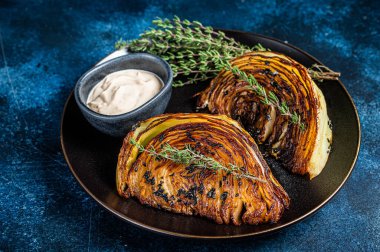 Fried cabbage steaks with sauce on a black plate. Blue background. Top view.