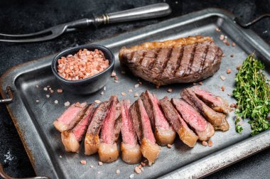 Kızarmış ve dilimlenmiş Top sığır filetosu bifteği, ızgara biftek çelik servis tepsisinde baharatlı biftek. Siyah arka plan. Üst görünüm.