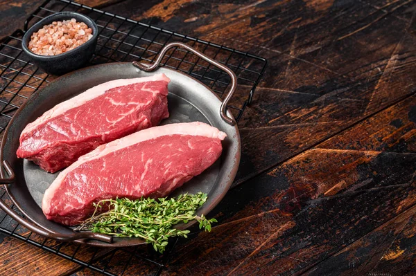 Raw top sirloin steak, cap rump beef meat steak on kitchen tray with spices. Wooden background. Top view. Copy space.
