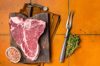 Biftek, biftek, kekik ve ahşap tahtada deniz tuzu. Turuncu arka plan. Üst görünüm.