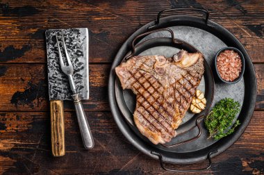 Barbekü ızgara T-bone ya da çelik tepside biftek ve şifalı otlar. Ahşap arka plan. Üst görünüm.