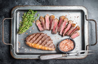 Fried and sliced Top sirloin steak, Grilled cup rump beef meat steak on a steel serving tray with spices. Black background. Top view. clipart