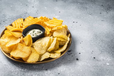 Variety of Potato chips in a plate served with dip sauce. Gray background. Top view. Copy space.