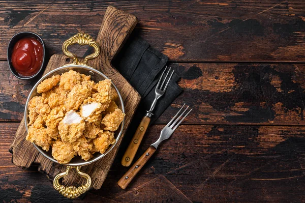 Homemade Crispy Popcorn Chicken bites in a skillet. Wooden background. Top view. Copy space.