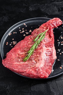 Seasoned raw tri-tip beef meat steak on plate. Black background. Top view.