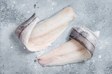 Mutfak masasında iki çiğ mezgit balığı filetosu. Gri arka plan. Üst görünüm.