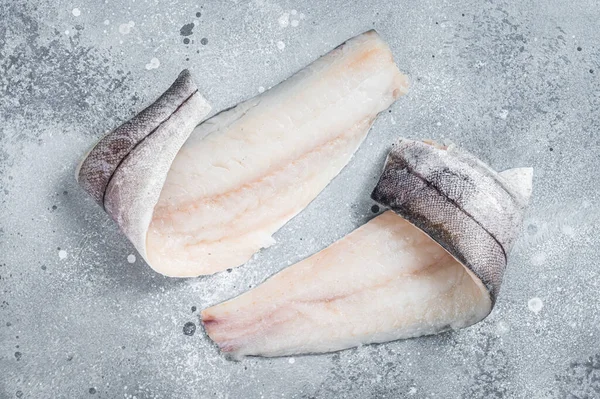 Mutfak masasında iki çiğ mezgit balığı filetosu. Gri arka plan. Üst görünüm.