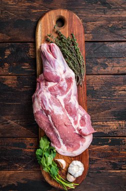 Raw lamb whole shoulder, fresh leg meat on a wooden board with spices. Wooden background. Top view.