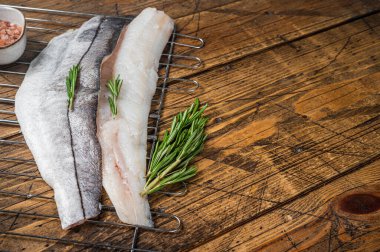 Raw fish fillets on grill with rosemary and herbs. Wooden background. Top view. Copy space.