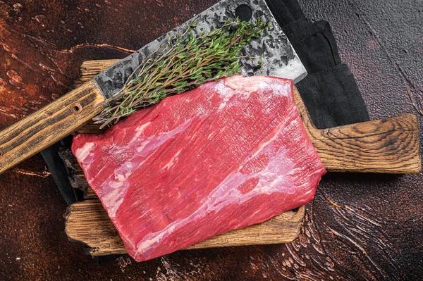 Alternative raw flap flank beef meat steak on butcher board. Dark background. Top view.
