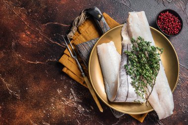 Whitefish fillet, raw Haddock fish on plate with rosemary and thyme. Dark background. Top view. Copy space.