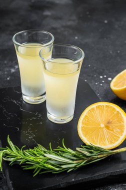 Traditional italian lemon alcohol drink liqueur limoncello with lemon and rosemary. Black background. Top view.