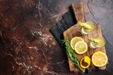 Italian limoncello liqueur and fresh lemons on a rustic wooden board. Dark background. Top view. Copy space.