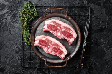 Raw fresh lamb loin chops with herbs and spices in steel tray. Black background. Top view.