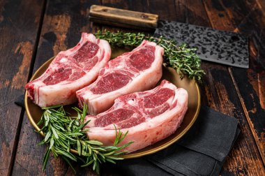Uncooked Raw lamb loin chops steaks, saddle in plate with rosemary and thyme. Wooden background. Top view.